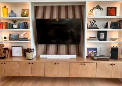 Modern living room with a TV, wooden shelves, books, plants, art, and a record player on a cabinet.