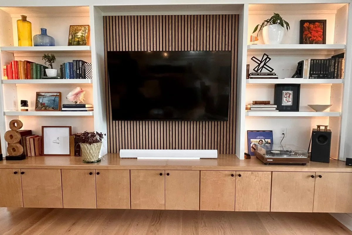 Modern living room with a TV, wooden shelves, books, plants, art, and a record player on a cabinet.