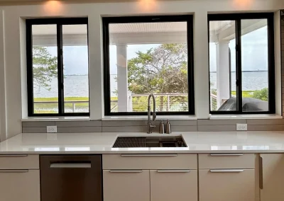 Modern kitchen with white cabinets, a sink, and large windows overlooking a lake and trees outside.