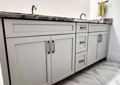 Light gray double-sink vanity with granite countertop and hexagon tile floor in a modern bathroom.