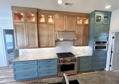 Modern kitchen with wood and blue cabinets, stainless stove, hood, microwave, and white tile backsplash.