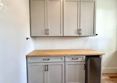 Gray cabinets and drawers with a wood countertop and mini fridge, set against a white wall and wood floor.