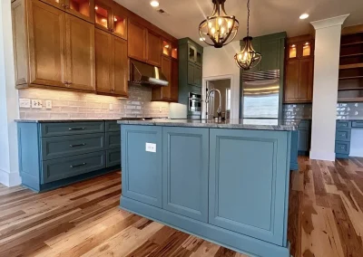 Modern kitchen with blue island, wood cabinets, pendant lights, stainless appliances, and wood flooring.