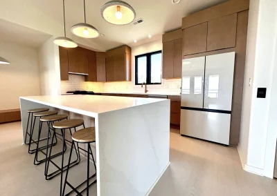 Modern kitchen with wood cabinets, white countertops, island with stools, and three pendant lights.