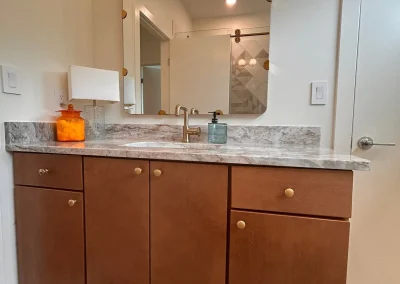 Bathroom vanity with brown cabinets, marble countertop, modern faucet, and a lighted mirror above.