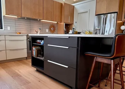 Modern kitchen with wood cabinets, black island, pendant lights, bar stool, and stainless steel refrigerator.