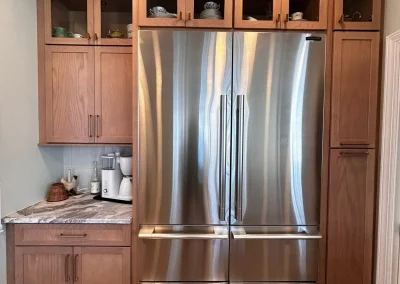 Large stainless steel refrigerator surrounded by wooden cabinets and a small countertop with kitchen appliances.