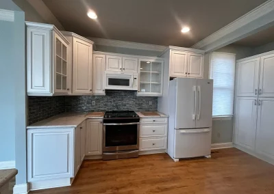 Modern kitchen with white cabinets, stainless steel oven, white fridge, and gray tile backsplash.