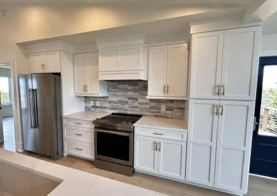 Modern kitchen with white cabinets, stainless steel appliances, and a gray tile backsplash.