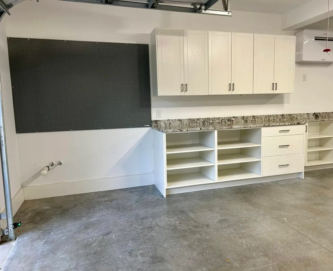 Garage with white cabinets, open shelves, granite countertop, and empty pegboard on the wall.