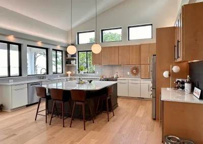 Modern kitchen with wood cabinets, island seating, pendant lights, and large windows letting in natural light.