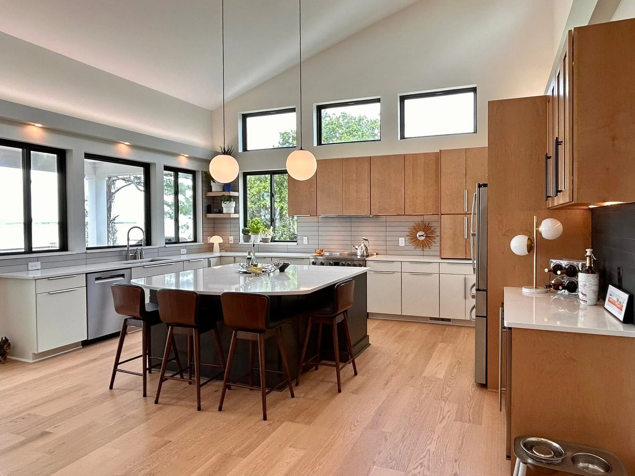 Modern kitchen with wood cabinets, island seating, pendant lights, and large windows letting in natural light.