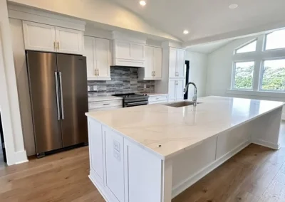 Modern kitchen with white cabinets, large island, stainless steel fridge, and wood floors.