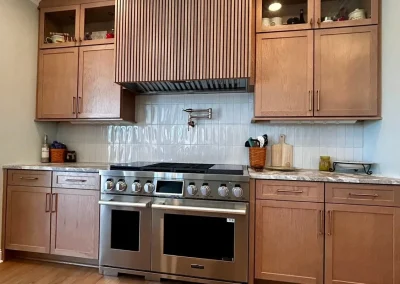 Modern kitchen with wooden cabinets, marble countertop, large stove, and a backsplash with white tiles.