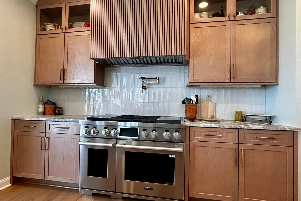 Modern kitchen with wooden cabinets, marble countertop, large stove, and a backsplash with white tiles.