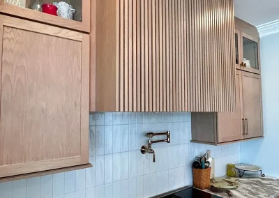 Modern kitchen with wood cabinets, a marble countertop, gas stove, and a wall-mounted pot filler above the range.