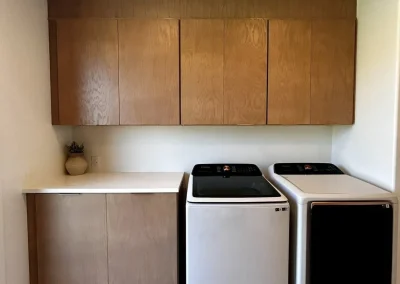Modern laundry room with light wood cabinets, a countertop, and a washer and dryer side by side.