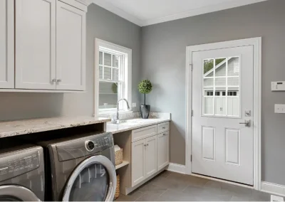 Modern laundry room with washer, dryer, sink, white cabinets, and a gray door with window.