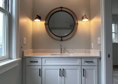 Modern bathroom vanity with marble countertop, round mirror, two lights, and hexagon floor tiles.