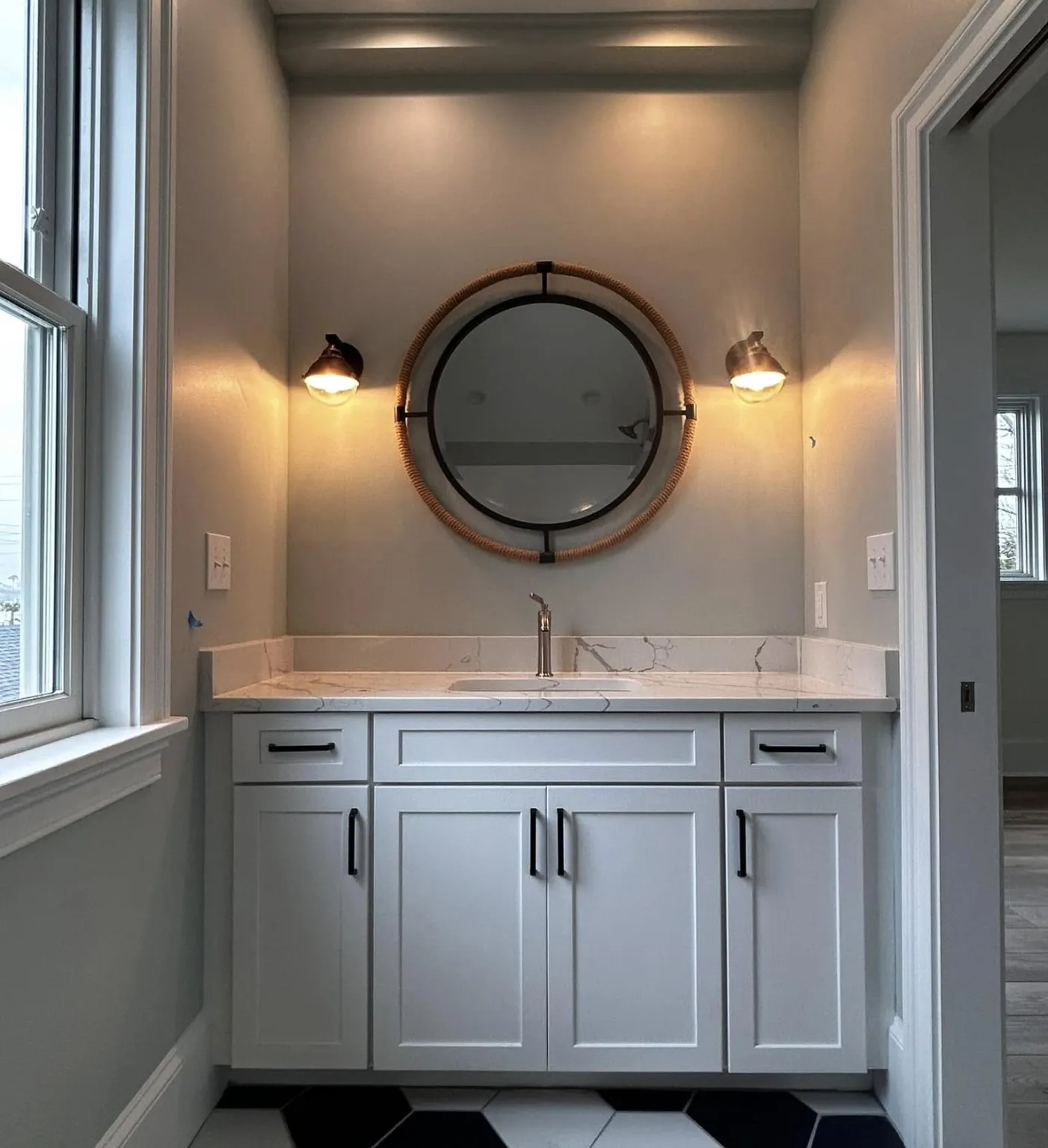 Modern bathroom vanity with marble countertop, round mirror, two lights, and hexagon floor tiles.