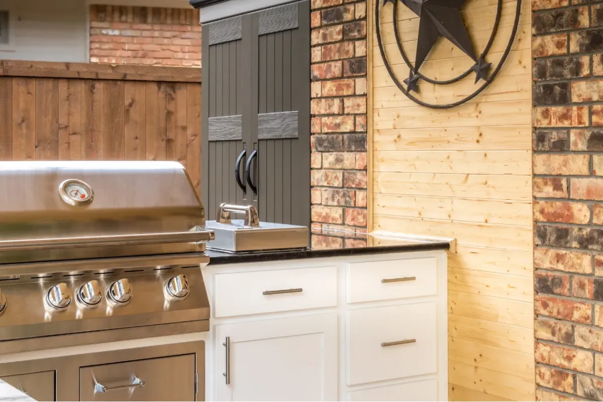 Outdoor kitchen with a grill, sink, cabinets, and a metal star decor on a brick and wood wall.
