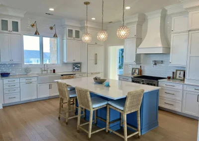 Modern kitchen with white cabinets, blue island, wicker chairs, pendant lights, and wood floors.