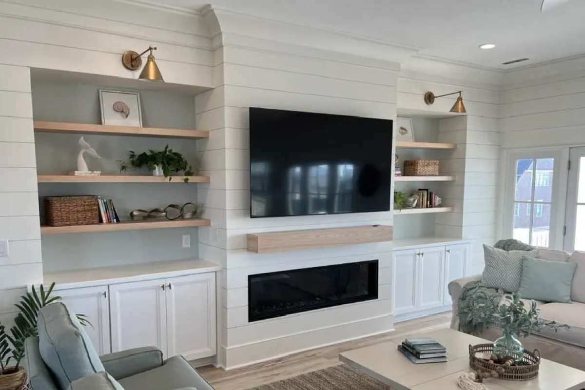 A modern living room with a wall-mounted TV, fireplace, shelves, and cabinets with decor and plants.